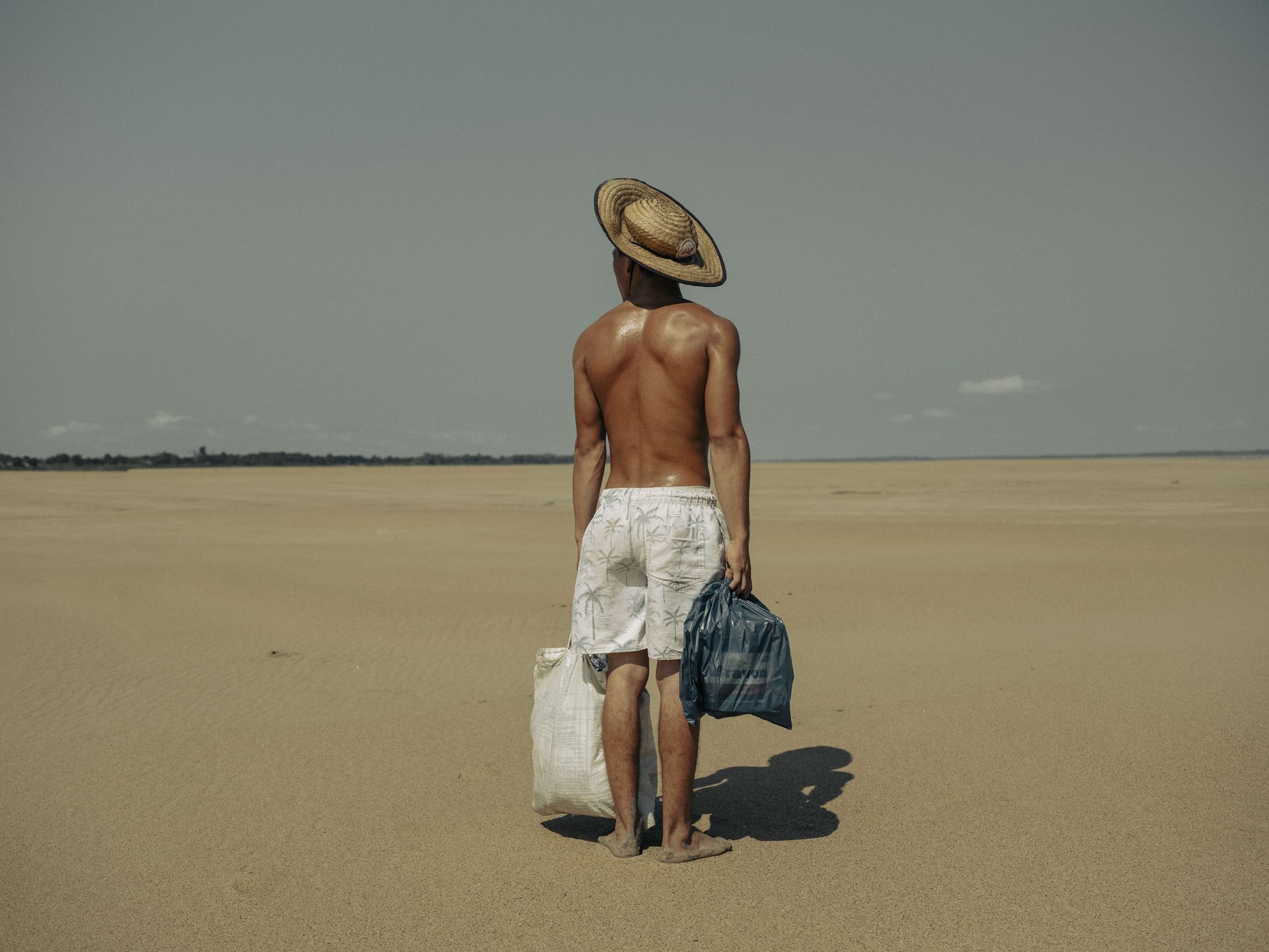 A young man brings food to his mother who lives in the village of Manacapuru, Amazonas, Brazil. The village was once accessible by boat, but because of the drought, he must walk two kilometers along the dry riverbed of the Solimões River to reach her.